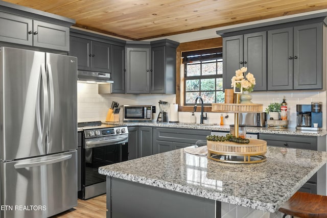 kitchen featuring appliances with stainless steel finishes, sink, gray cabinetry, a center island, and light stone countertops