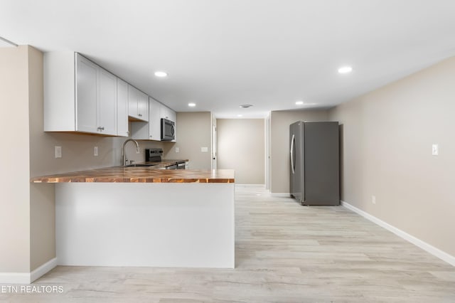 kitchen featuring butcher block countertops, sink, kitchen peninsula, stainless steel appliances, and light hardwood / wood-style flooring