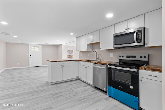 kitchen with appliances with stainless steel finishes, butcher block counters, sink, white cabinets, and kitchen peninsula