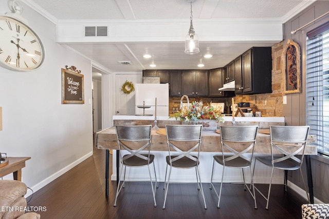 kitchen featuring a breakfast bar area, dark hardwood / wood-style floors, dark brown cabinetry, ornamental molding, and white fridge