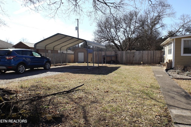 view of yard featuring a carport, fence, driveway, and a storage shed