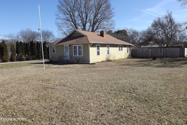 view of side of home featuring a yard, fence, a chimney, and a shingled roof