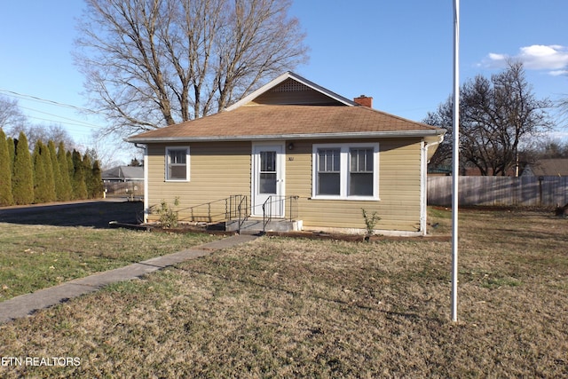 bungalow-style home with roof with shingles, a chimney, a front yard, and fence