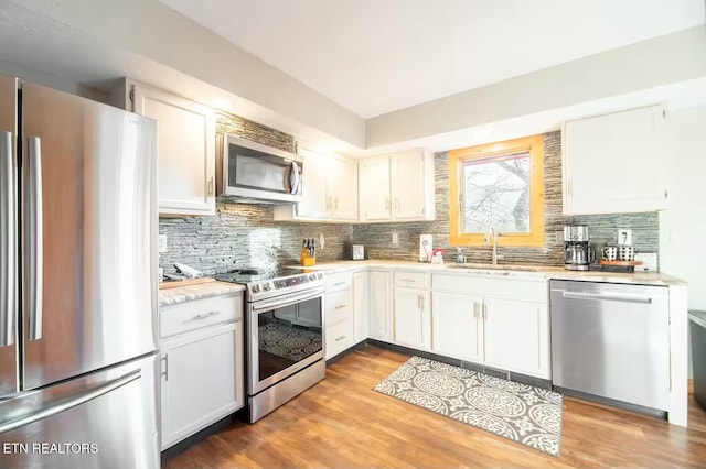 kitchen with sink, white cabinetry, tasteful backsplash, hardwood / wood-style flooring, and stainless steel appliances