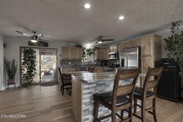 kitchen with light hardwood / wood-style flooring, ceiling fan, appliances with stainless steel finishes, backsplash, and kitchen peninsula