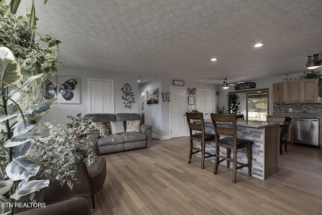 living room featuring ceiling fan, a textured ceiling, and light wood-type flooring