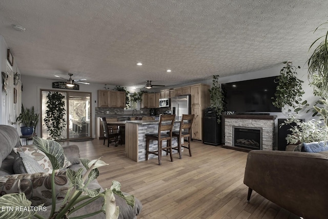 living room with a fireplace, sink, ceiling fan, light hardwood / wood-style floors, and a textured ceiling