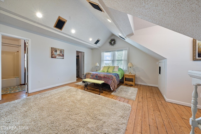 bedroom with light hardwood / wood-style floors, vaulted ceiling, and a textured ceiling