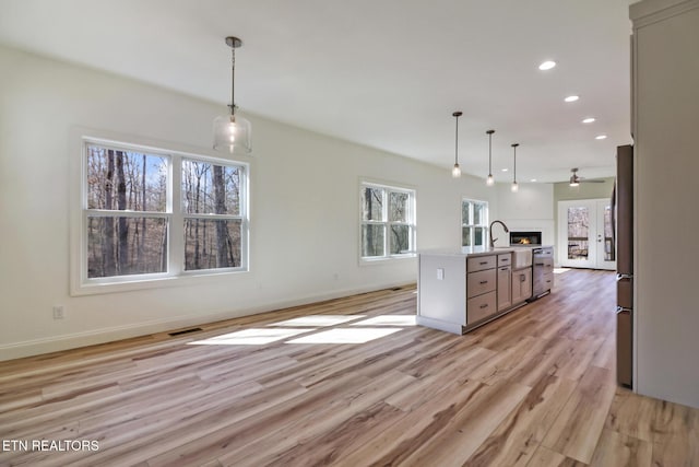 kitchen featuring hanging light fixtures, stainless steel appliances, a center island with sink, and light hardwood / wood-style flooring