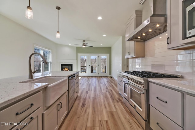 kitchen with pendant lighting, sink, appliances with stainless steel finishes, light stone counters, and wall chimney exhaust hood