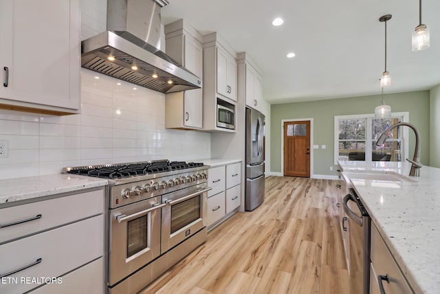 kitchen featuring pendant lighting, appliances with stainless steel finishes, range hood, light stone counters, and tasteful backsplash