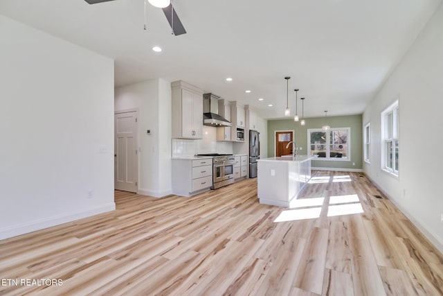 kitchen with appliances with stainless steel finishes, backsplash, an island with sink, decorative light fixtures, and wall chimney exhaust hood