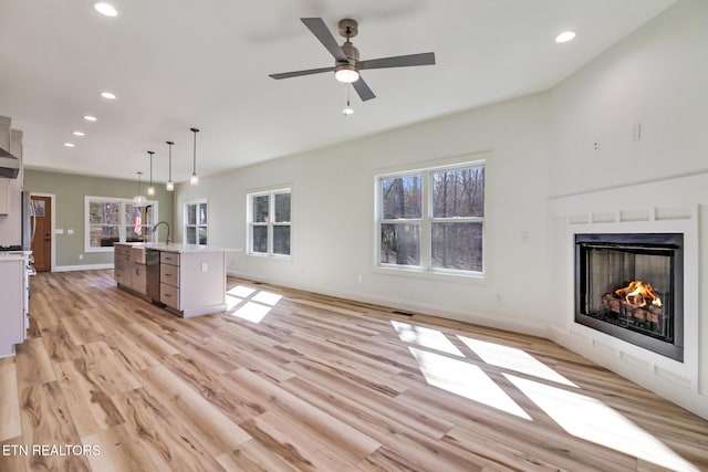 unfurnished living room featuring ceiling fan, sink, and light wood-type flooring