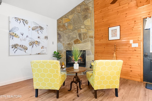 living area with a fireplace, vaulted ceiling, wood walls, and hardwood / wood-style flooring