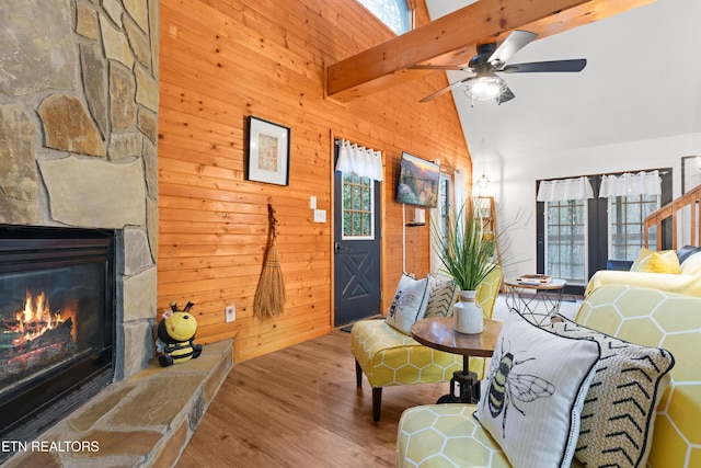 living room featuring beam ceiling, a stone fireplace, high vaulted ceiling, hardwood / wood-style floors, and wooden walls