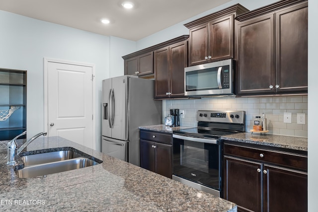 kitchen with appliances with stainless steel finishes, tasteful backsplash, sink, dark stone counters, and dark brown cabinetry