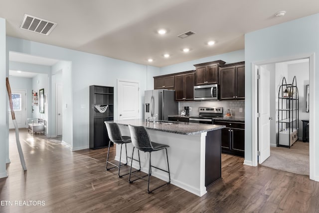 kitchen with appliances with stainless steel finishes, tasteful backsplash, an island with sink, a breakfast bar area, and dark stone countertops