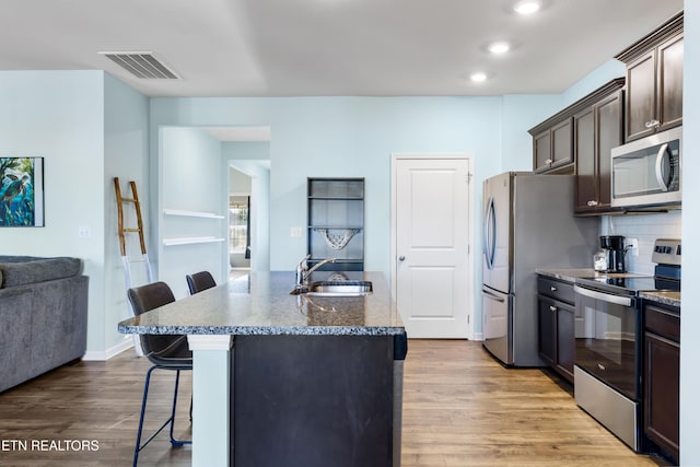 kitchen featuring sink, light hardwood / wood-style flooring, a breakfast bar area, appliances with stainless steel finishes, and an island with sink