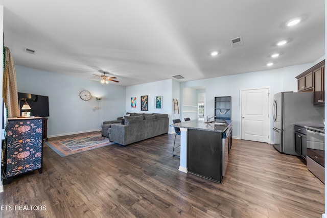 kitchen with dark brown cabinetry, stone countertops, a center island with sink, a kitchen breakfast bar, and stainless steel appliances