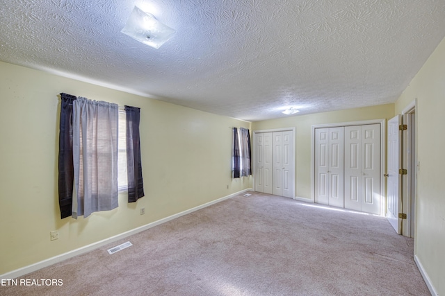 unfurnished bedroom with light carpet, two closets, and a textured ceiling