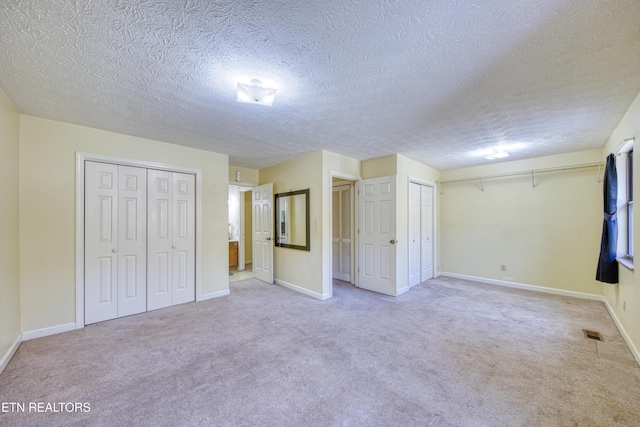 unfurnished bedroom featuring multiple closets, carpet, and a textured ceiling