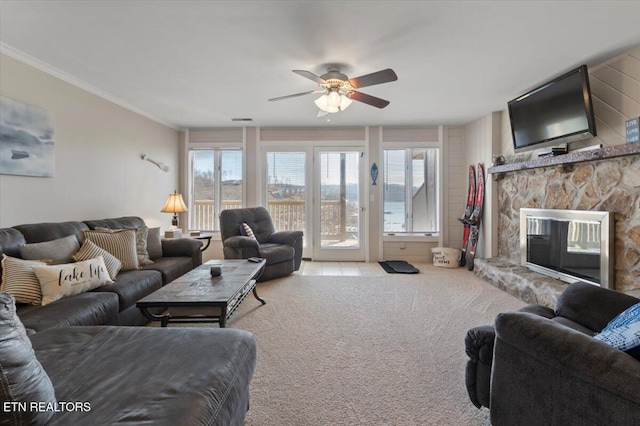 living room with light carpet, a stone fireplace, ornamental molding, and ceiling fan