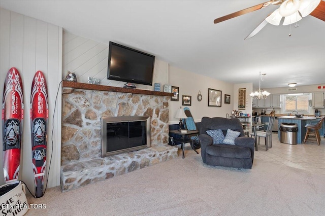 living room with a stone fireplace, ceiling fan with notable chandelier, and light carpet