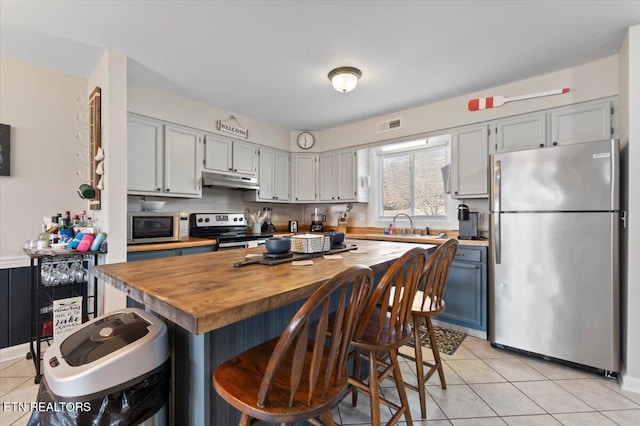 kitchen with appliances with stainless steel finishes, a breakfast bar area, light tile patterned floors, and wood counters