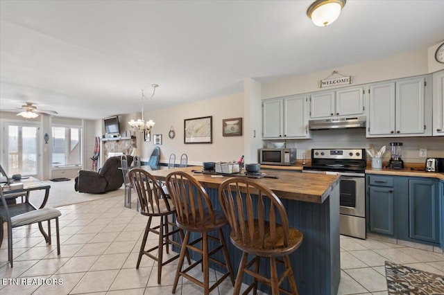 kitchen featuring light tile patterned floors, appliances with stainless steel finishes, butcher block counters, hanging light fixtures, and ceiling fan with notable chandelier