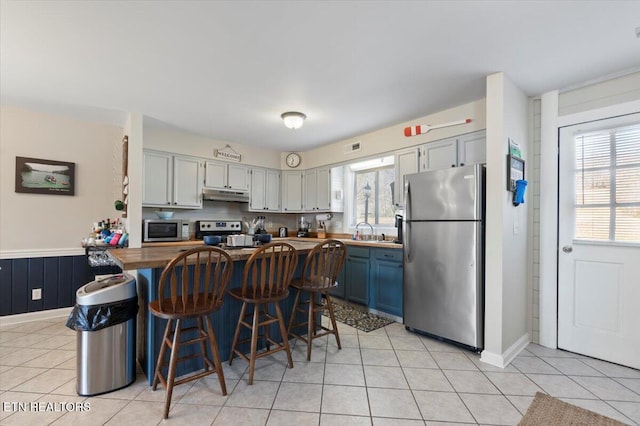 kitchen featuring sink, blue cabinetry, appliances with stainless steel finishes, a kitchen bar, and wood counters