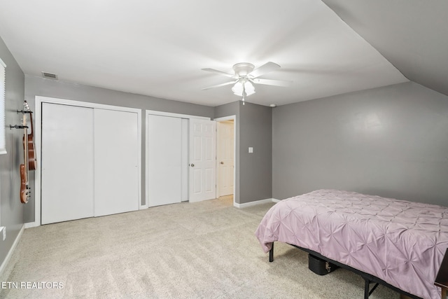 bedroom featuring ceiling fan, light colored carpet, and multiple closets