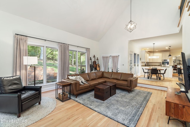 living room featuring high vaulted ceiling, a chandelier, and light hardwood / wood-style floors