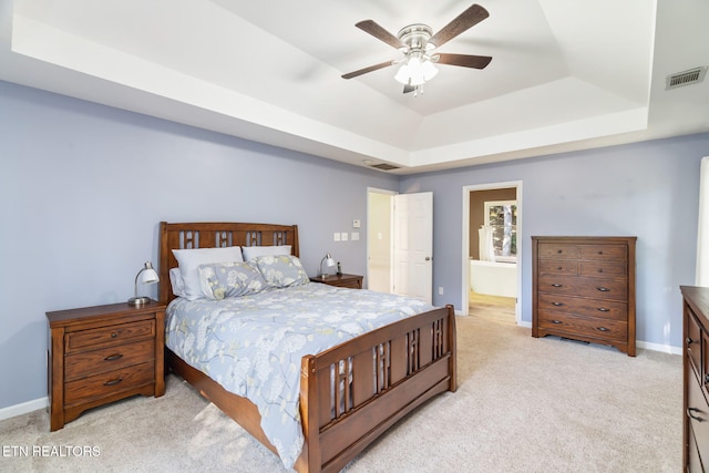 bedroom with light carpet, a tray ceiling, ceiling fan, and ensuite bathroom