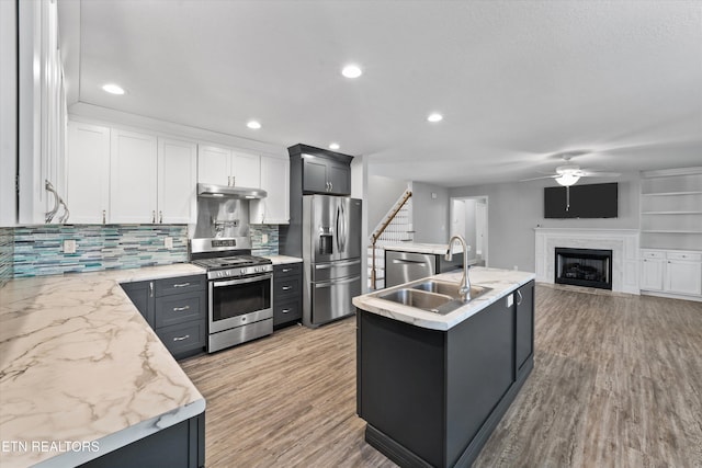 kitchen with sink, white cabinetry, stainless steel appliances, a center island with sink, and light wood-type flooring