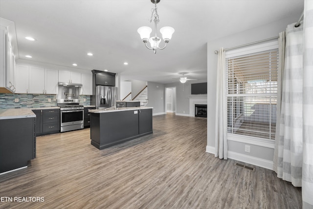 kitchen featuring backsplash, stainless steel appliances, a center island, white cabinets, and decorative light fixtures