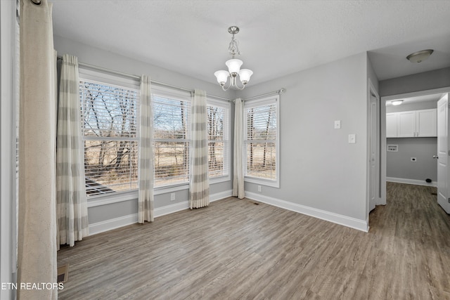 unfurnished dining area with a notable chandelier, light hardwood / wood-style floors, and a textured ceiling