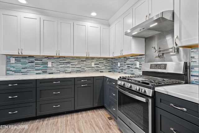 kitchen featuring ventilation hood, white cabinets, gas stove, light stone countertops, and light wood-type flooring