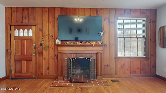 unfurnished living room featuring wood-type flooring, a brick fireplace, and wood walls