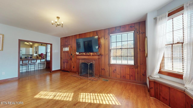 unfurnished living room featuring a brick fireplace, a notable chandelier, light hardwood / wood-style floors, and wood walls