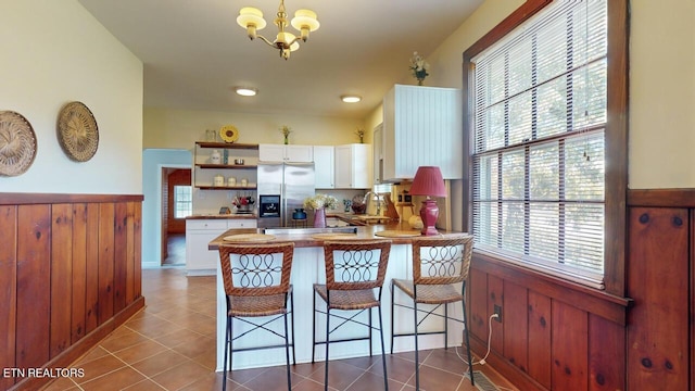 kitchen featuring decorative light fixtures, stainless steel fridge, kitchen peninsula, and white cabinets