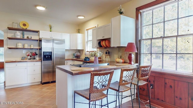 kitchen with a kitchen bar, light tile patterned floors, stainless steel fridge, kitchen peninsula, and white cabinets