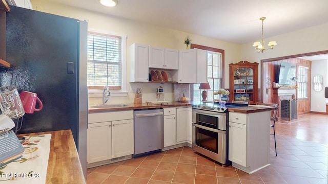 kitchen with sink, appliances with stainless steel finishes, white cabinetry, light tile patterned flooring, and decorative light fixtures