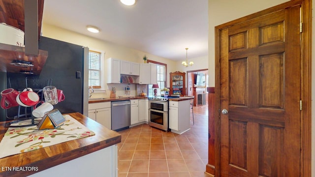 kitchen with light tile patterned floors, an inviting chandelier, stainless steel appliances, white cabinets, and decorative light fixtures