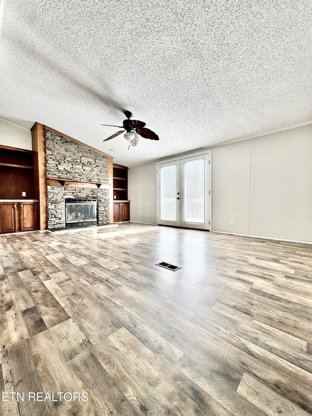 unfurnished living room featuring french doors, a stone fireplace, a textured ceiling, ceiling fan, and light hardwood / wood-style floors