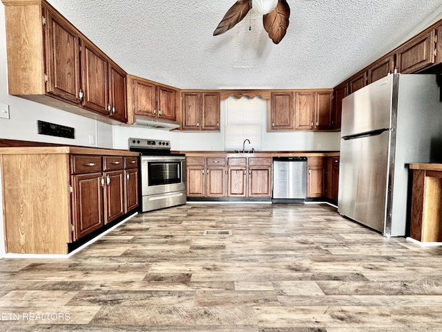 kitchen featuring appliances with stainless steel finishes, sink, ceiling fan, light hardwood / wood-style floors, and a textured ceiling