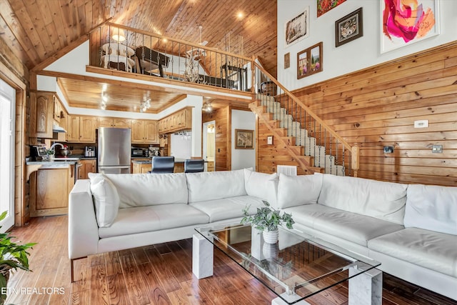 living room with high vaulted ceiling, wooden walls, sink, hardwood / wood-style flooring, and wood ceiling