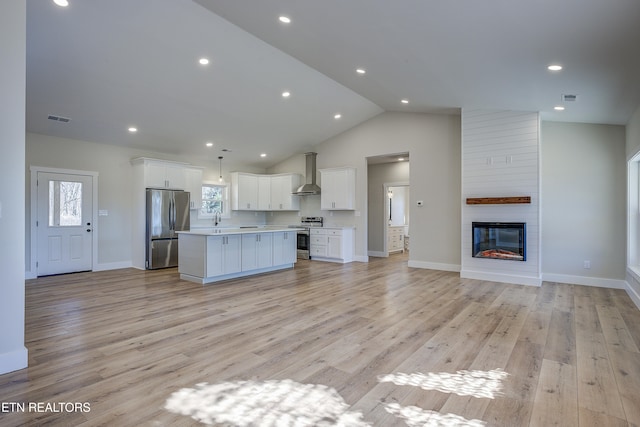 kitchen featuring wall chimney range hood, appliances with stainless steel finishes, white cabinets, a kitchen island, and light wood-type flooring