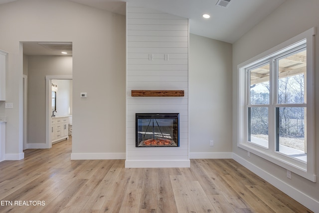 unfurnished living room with lofted ceiling, a large fireplace, and light hardwood / wood-style flooring