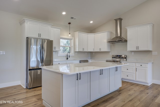 kitchen with stainless steel appliances, white cabinetry, a kitchen island, and wall chimney range hood