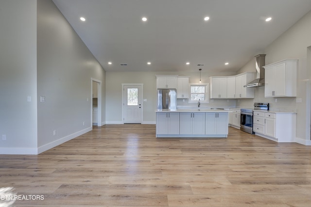 kitchen with wall chimney range hood, a center island, white cabinets, and appliances with stainless steel finishes